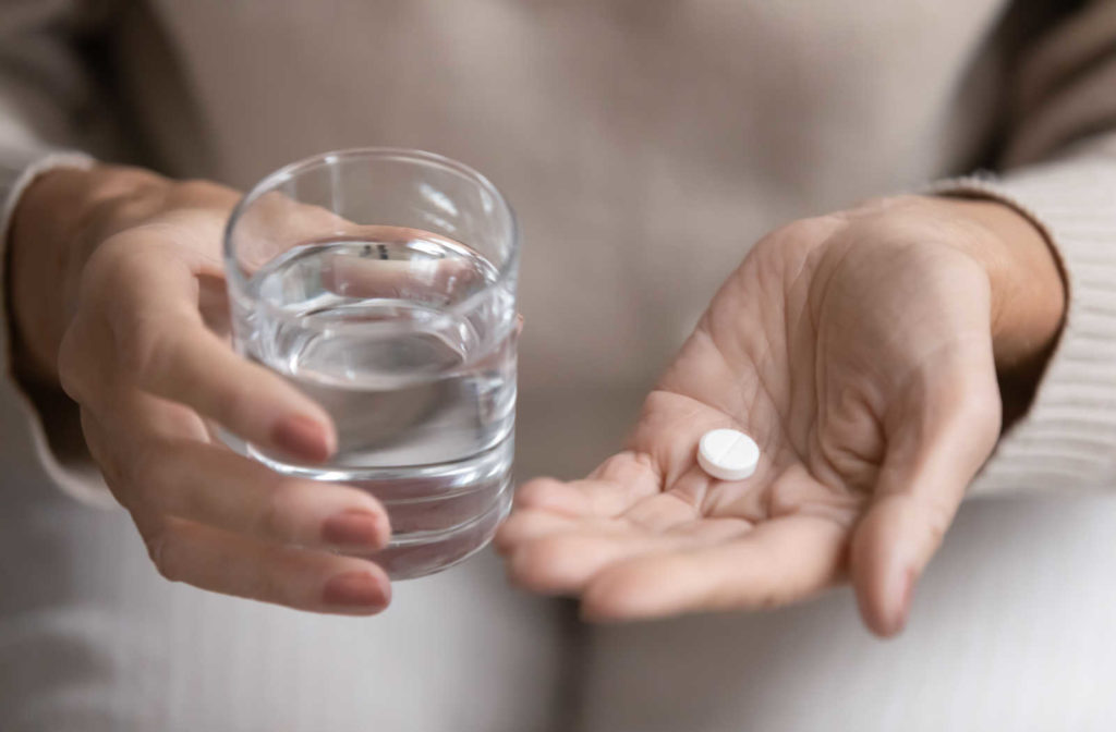 A close-up top view of a woman holding a glass of water and a sedative pill administered by a dentist at the dental clinic.
