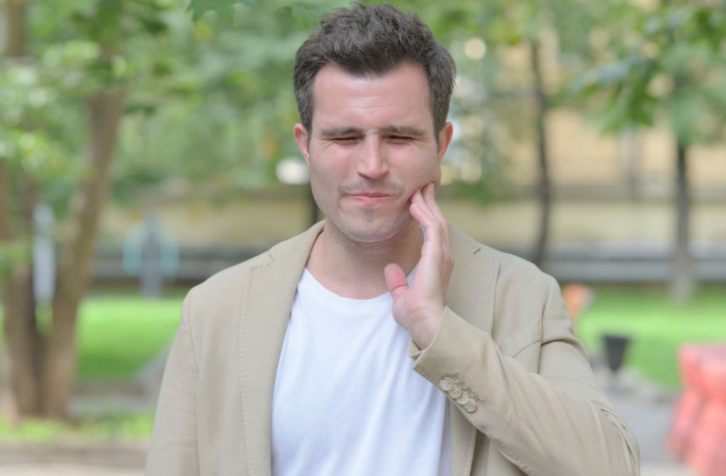 A man walking in a park suffering from oral pain holds his left cheek with his left hand.